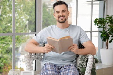 Evdeki koltukta kitap okuyan yakışıklı adam.