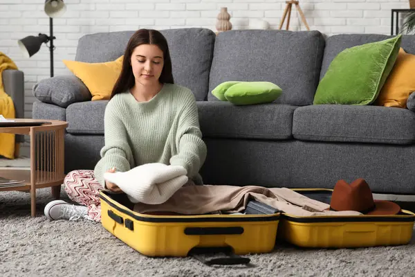 Evde genç bir kadın bavulunu bavula koyup yere yığıyor. Seyahat kavramı