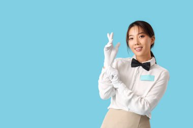 Mavi arka planda beyaz eldivenli, gülümseyen genç Asyalı garson.