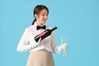 Mavi arka planda şarap ve cam şişesiyle gülümseyen genç Asyalı garson.