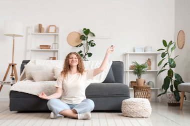 Klimalı, uzaktan kumandalı gülümseyen genç kadın evde yerde oturuyor.