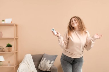 Uzaktan kumandalı ve kremli gülümseyen genç kadın oturma odasında.