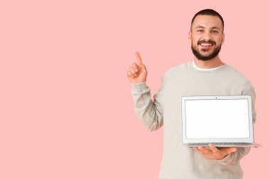 Pembe arka planda parmak ve dizüstü bilgisayarı olan genç bir adam.