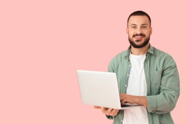 Pembe arka planda dizüstü bilgisayarı olan genç bir adam.