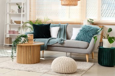 Gri kanepe, masa ve puflarla aydınlık oturma odasının içinde.