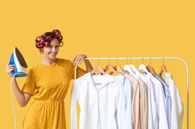 Sarı arka planda, askıların yanında demir tutan genç bir kadın.