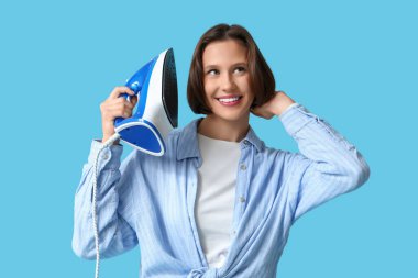 Mavi arka planda demiri olan gülümseyen genç kadın.