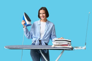 Mavi arka planda giysileri ütüleyen genç kadın.