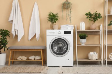 Rafların, çamaşır makinesinin ve gri bankın olduğu şık bir banyo.