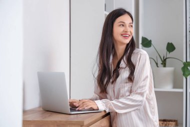 Çizgili pijamalı kadın evde klozette dizüstü bilgisayarla çalışıyor.