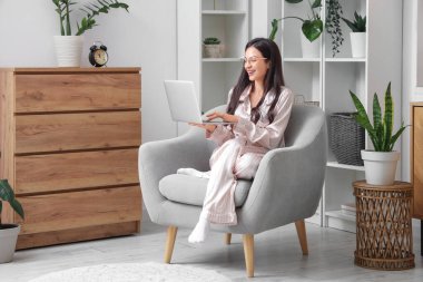 Çizgili pijamalarıyla evde dizüstü bilgisayarla çalışan serbest çalışan bir kadın.