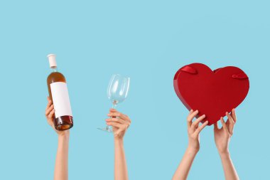 Kalp şeklinde hediye kutusu, cam ve şarap şişesi mavi arka planda olan kadın elleri. Sevgililer Günü kutlaması