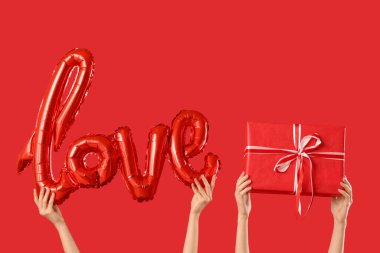 Balon şekilli kadın elleri. Aşk kelimesi ve kırmızı arka planda hediye kutusu. Sevgililer Günü kutlaması
