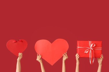 Kağıt kalpli kadın eller ve kırmızı arka planda hediye kutuları. Sevgililer Günü kutlaması
