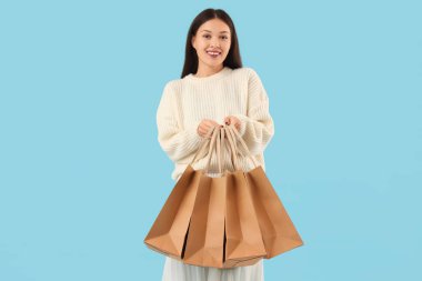 Mavi arka planda alışveriş torbaları olan mutlu genç bir kadın.