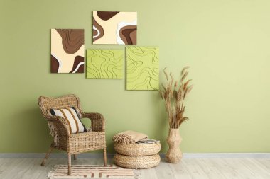 Hasır koltuk, vazodaki otlar ve odadaki yeşil duvardaki tablolar.