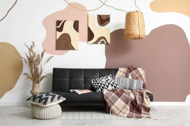 Rahat bir kanepe, yastıklı bir puf ve odanın renkli duvarlarında resimler.