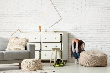 Deprem sırasında oturma odasında göğsünün yanındaki çekmeceleri kapatan korkmuş genç kadın.