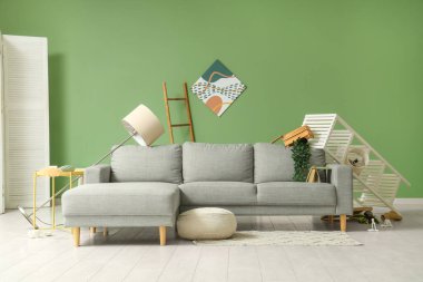 Gri kanepeli dağınık oturma odasının içi, rafları alt üst edilmiş ve depremden sonra etrafa saçılmış eşyalar.