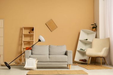 Gri kanepeli dağınık oturma odasının içi, standart lambayı ters çevirmiş ve depremden sonra rafları eğmiş.