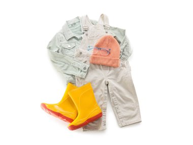 Beyaz arka planda şık çocuk kıyafetleri, lastik botları ve gözlükleri var.