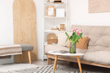 Oturma odasının içinde kanepe, raf ünitesi, güzel lale çiçekleri ve sehpanın üzerinde dergiler.