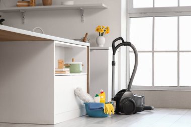 Mutfakta yerde temizlik malzemeleri ve elektrik süpürgesi olan plastik bir leğen.