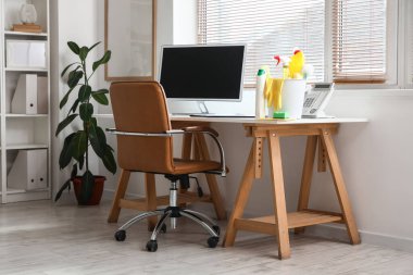 Modern ofisteki plastik kovada temizlik malzemeleri ve bilgisayar var.