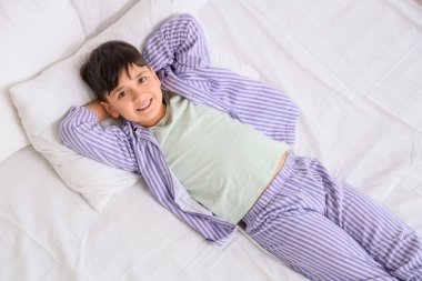 Çizgili pijama giymiş yakışıklı bir çocuk. Yatakta yatıyor.
