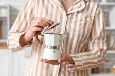 Evde gayzer kahve makinesiyle pijamalı genç bir kadın, yakın plan.