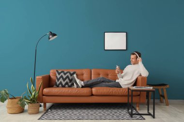 Evdeki kahverengi koltukta cep telefonu kullanan kulaklıklı yakışıklı bir genç.