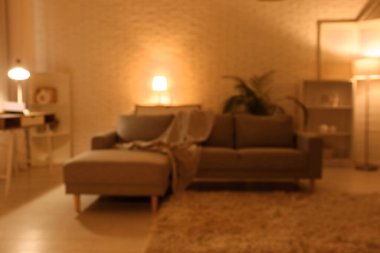 Gece oturma odasının içinde kanepe, raf üniteleri, parlayan lambalar ve işyeri, bulanık görüş.