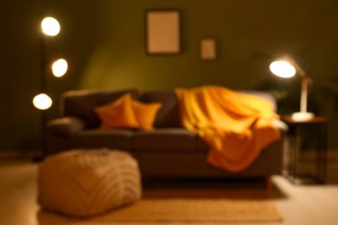 Gece oturma odasının içi, kanepe, puf ve yeşil duvarın yanında parlayan lambalar, bulanık manzara.