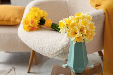Oturma odasındaki koltuğa karşı sehpanın üzerinde narsis çiçekleri olan vazo, yakın plan.