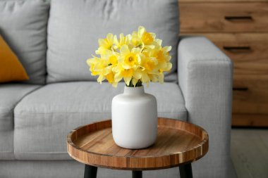 Oturma odasındaki kanepeye karşı sehpanın üzerinde narsis çiçekleri olan vazo, yakın plan.