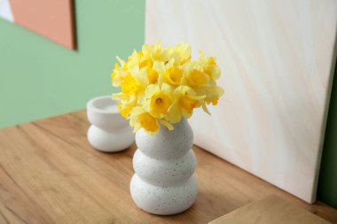 Oturma odasındaki yeşil duvarın yanındaki dolapta narsist çiçekleri ve dekoru olan vazo.