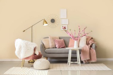 Oturma odasının içinde kanepe, pembe koltuk ve vazoda çiçek açan dallar var.