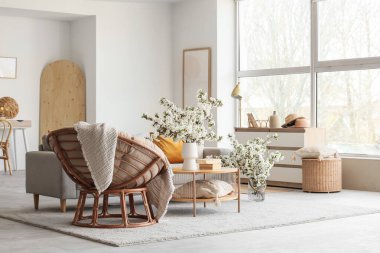 Kanepe, koltuk ve vazolarda çiçek açan dallarla aydınlık oturma odasının içinde.