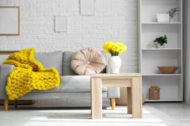 İçinde kanepe, raf ünitesi ve vazoda narsisleri olan oturma odası.