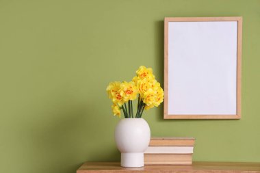 Vazosu narsisli ve kitapları yeşil duvarın yanında, odada.