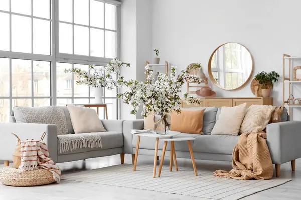 Kanepeleri ve vazolarında çiçek açan dalları olan aydınlık oturma odasının içinde.