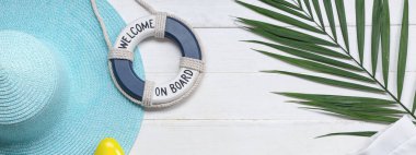 Plaj aksesuarlarından yapılmış çerçeve, dekoratif can simidi ve beyaz ahşap arka planda güneş kremi.