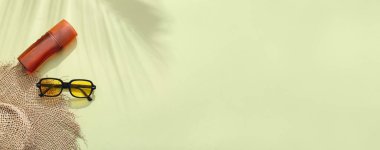 Yeşil arka planda güneş gözlüğü, şapka ve güneş kremi.