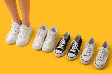 Sarı arka planda farklı şık spor ayakkabıları olan genç bir kadının bacakları.