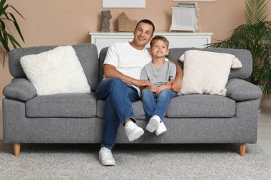 Mutlu bir baba ve küçük oğlu evdeki kanepede oturuyor.