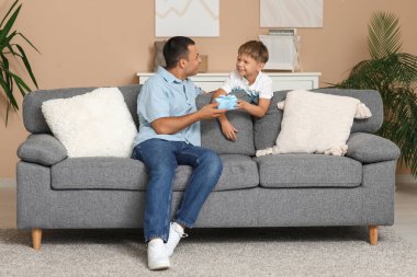 Mutlu küçük oğul, evde kanepede babasına hediye kutusuyla selam veriyor.