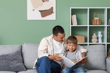 Mutlu baba ve küçük oğlu evdeki kanepede kitap okuyorlar.