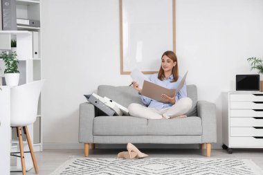 Ofisteki koltukta evrak klasöründe çalışan genç bir iş kadını.