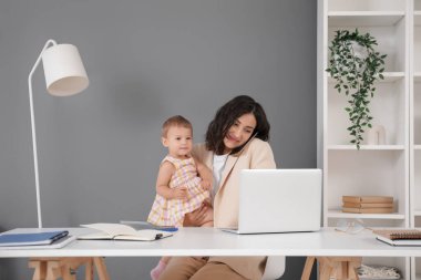 Çalışan anne evde bebeğiyle cep telefonuyla konuşuyor.