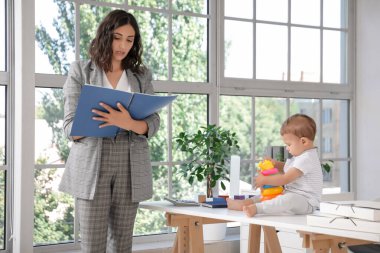 Dosyayla çalışan anne ve küçük bebeği ofiste masada oynuyorlar.